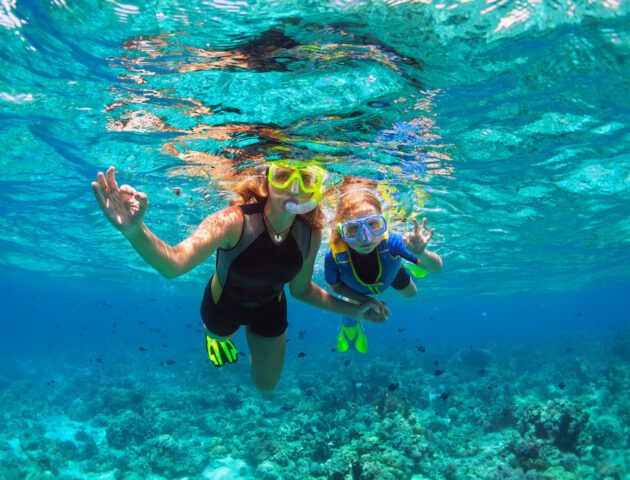 Mother, kid in snorkeling mask dive underwater with tropical fishes